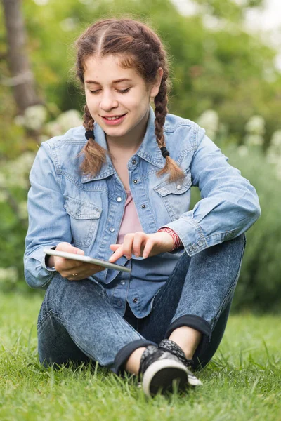 Genç kız yeşil baharda yatarken dijital tablet kullanıyor. — Stok fotoğraf