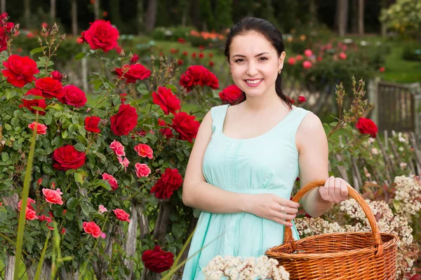 Portret van jonge vrouw met een mand in de buurt van rozen in de buitenlucht — Stockfoto