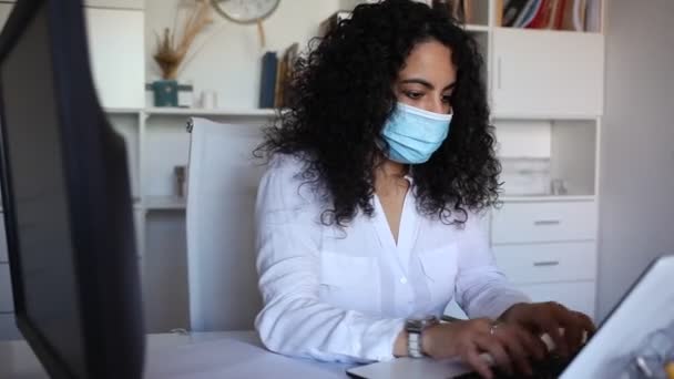 Женщина в защитной маске работает с документами и ноутбуком в офисе — стоковое видео