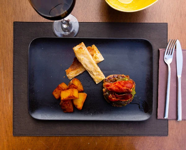 Traditionelle spanische Rissole mit Bratkartoffeln auf schwarzem Teller auf dem Tisch — Stockfoto