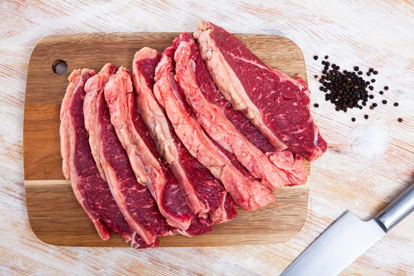 Pedaços de carne bovina com ervilhas de pimenta amarga na tábua de corte — Fotografia de Stock