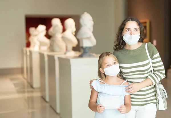 Petite fille et mère dans des masques protecteurs inspectent les expositions au musée — Photo