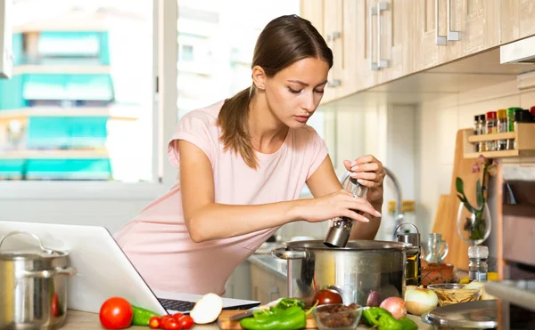 Hemmafru matlagning soppa och använda laptop — Stockfoto