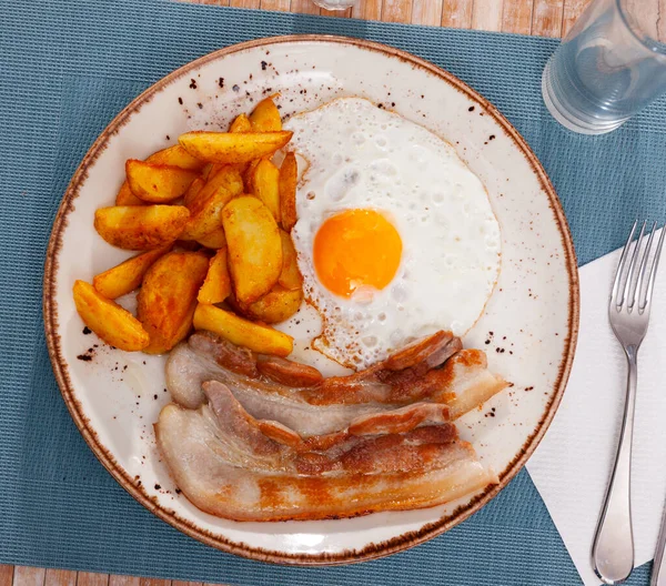 Grillezett sertéshús, sült burgonyával és tojással, kék tányéron tálalva, fa asztalon — Stock Fotó