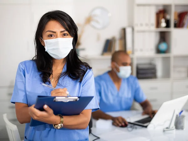 Женщина-врач в хирургической маске заполняет медицинскую форму — стоковое фото