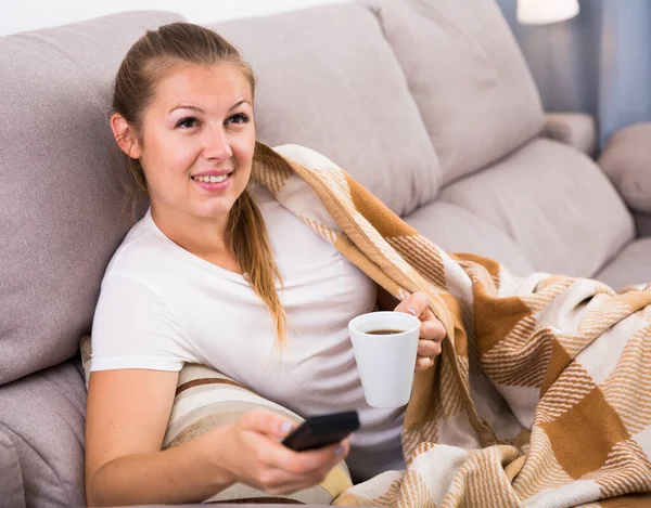 Ung kvinna tittar på TV och sitter med te — Stockfoto