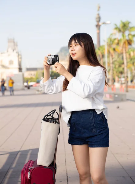 Sorrindo menina segurando câmera nas mãos e fotografando na cidade — Fotografia de Stock