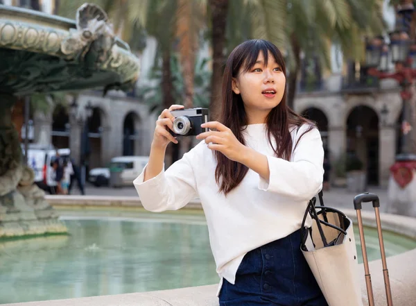 Joven viajera china paseando con equipaje por la ciudad, haciendo fotos de lugares de interés — Foto de Stock