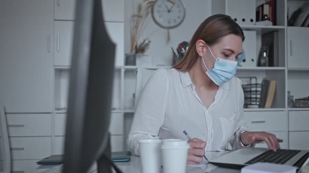 Mladá pracovnice nosí lékařskou masku obličeje zabývající se podnikatelskou činností v kanceláři Stock Video