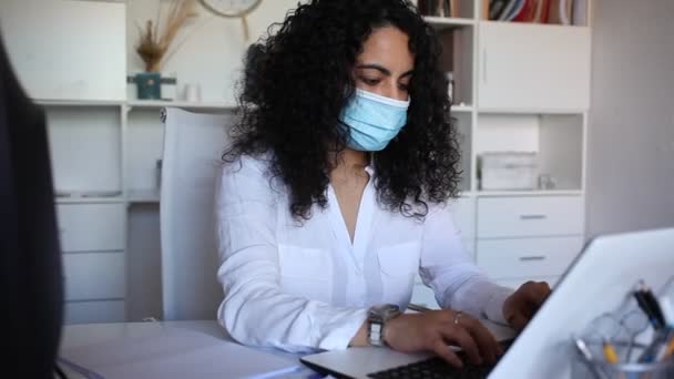 Portret van een zelfverzekerde jonge vrouw ondernemer in beschermende masker werken met computer en papieren in het kantoor — Stockvideo