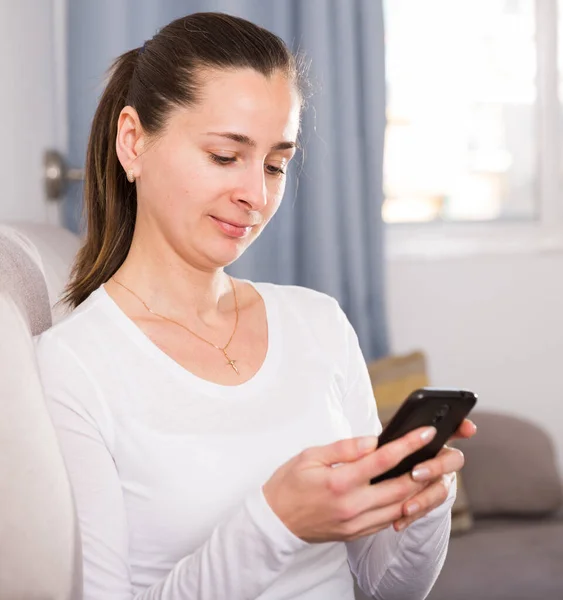 Giovane donna con un telefono cellulare sul divano di casa — Foto Stock