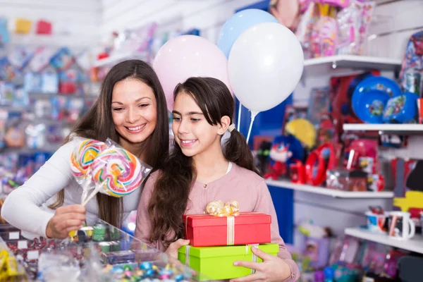 Mujer feliz con hija sosteniendo caramelos y regalos en la tienda —  Fotos de Stock