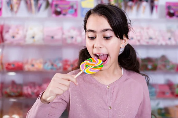 Small girl with lollipop on stick in sweet-shop — Stock Photo, Image