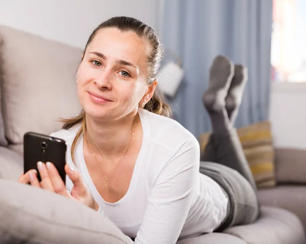 Jeune femme avec un téléphone portable sur le canapé à la maison — Photo