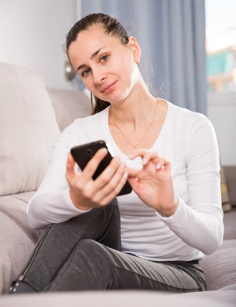 Молодая женщина с мобильным телефоном на диване дома — стоковое фото
