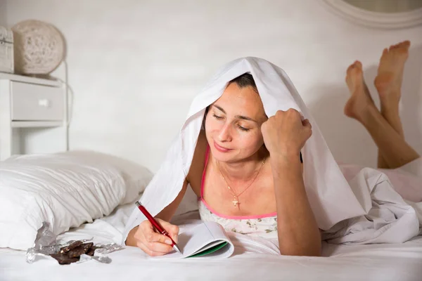 Mulher adulta escrevendo em diário e deitado na cama à noite — Fotografia de Stock