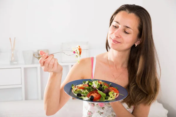 Mujer bonita positiva sosteniendo tenedor y comer ensalada de verduras en la cama —  Fotos de Stock