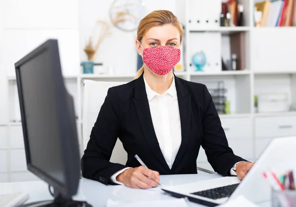 Affärskvinna i färgad medicinsk mask arbetar med bärbar dator — Stockfoto