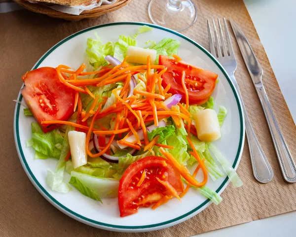 Mediterrán saláta paradicsommal, salátával és sárgarépával fehér tányéron a fa asztalon — Stock Fotó
