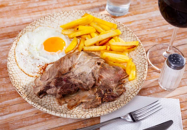 Close up χοιρινό ψητό με τηγανητές πατάτες και αυγό σερβίρεται σε μπλε πιάτο σε ξύλινο τραπέζι — Φωτογραφία Αρχείου