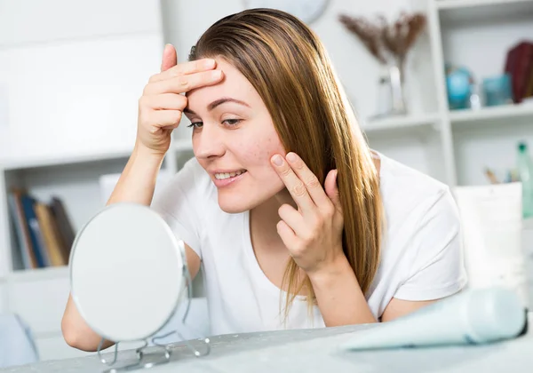 Smiling female is looking on her skin in the mirror — Stock Photo, Image