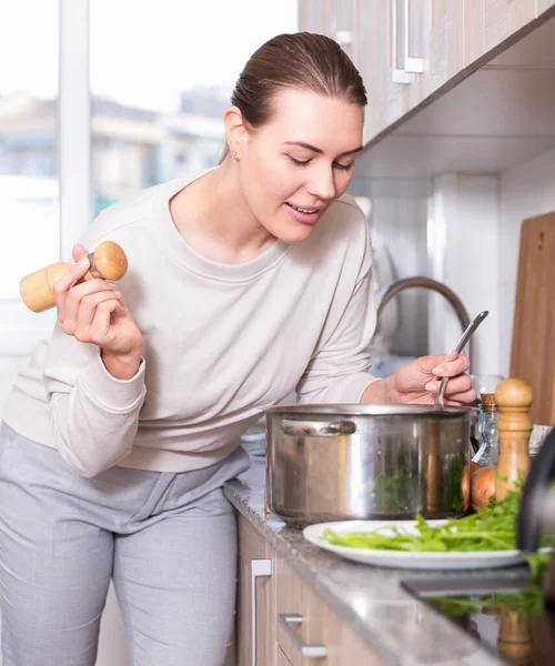 Femme gaie est debout près de la table avec de la marmite pour la soupe et le sel dans la cuisine — Photo