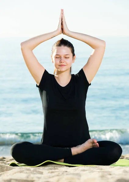 Mulher atlética em camiseta preta está sentada e praticando pranayama — Fotografia de Stock