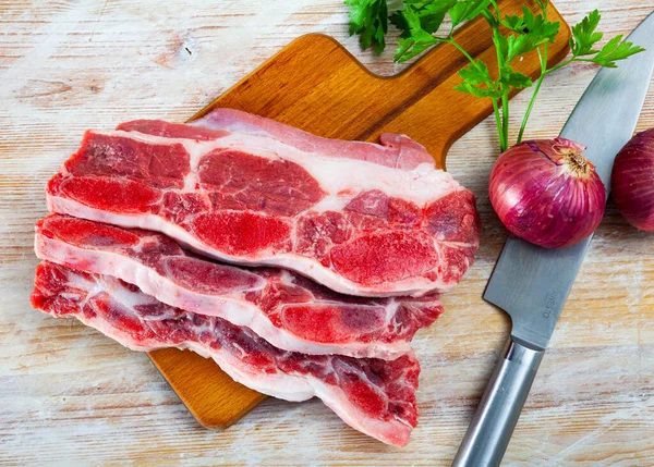 Κομμένες φέτες ωμού βοδινού κρέατος σε πιάτο κοπής με μπαχαρικά δίπλα του — Φωτογραφία Αρχείου