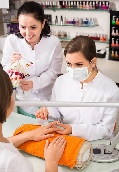 Neşeli tırnak teknisyeni kadın müşteriye güzellik salonunda oje rengini seçmesini öneriyor. — Stok fotoğraf