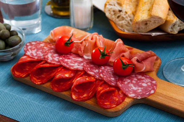 Comida sabrosa española rebanando salchichas y jamón con tomates en el escritorio de madera —  Fotos de Stock