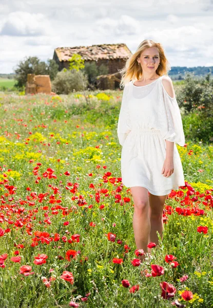 Junge Frau in weißem Kleid geht durch eine Mohnpflanze — Stockfoto