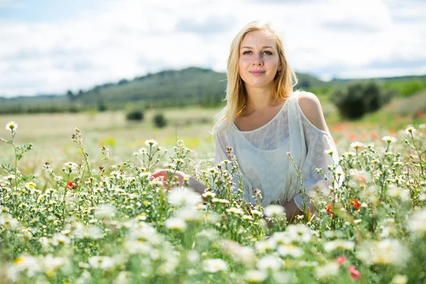 Ung flicka i vit klänning sitter i fält av vilda kamomill blommor — Stockfoto