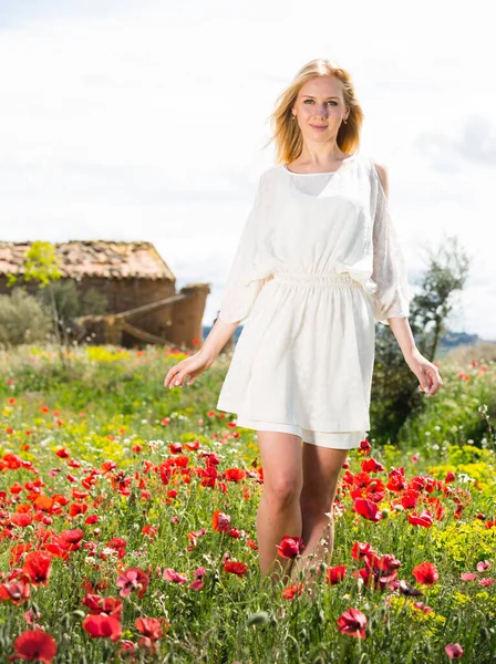 Γυναίκα φορώντας λευκό φόρεμα περπατώντας μέσα από ένα χωράφι παπαρούνας και απολαμβάνοντας — Φωτογραφία Αρχείου