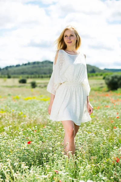 Hezká dívka v bílých šatech chůze na poli divoké heřmánku květiny — Stock fotografie