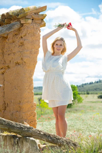 Frau in weißem Kleid posiert nahe Mauer mit Mohnblumen — Stockfoto