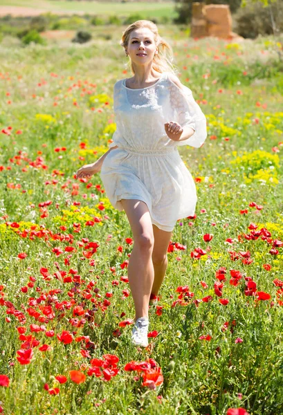 Chica alegre corriendo en el campo con plantas de amapolas —  Fotos de Stock