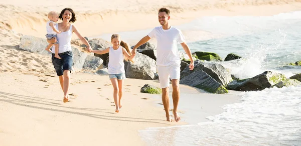 Eltern mit zwei Kindern joggen am Strand . — Stockfoto