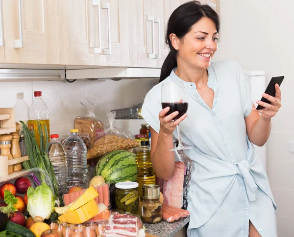 Fröhliche Frau plaudert pünktlich am Telefon und kocht in der Küche — Stockfoto