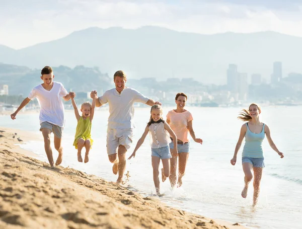 Большая активная семья счастливо бегает по пляжу — стоковое фото