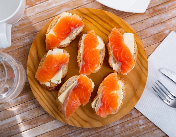 Fresh baguette with butter and salmon on wooden board — Stock Photo, Image