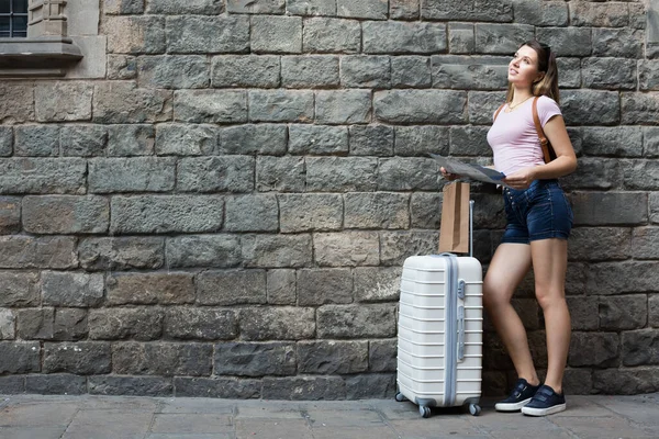 Glimlachende vrouw met reistas op stenen muurachtergrond — Stockfoto