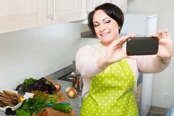 Retrato de ama de casa en delantal haciendo selfie en cocina doméstica —  Fotos de Stock