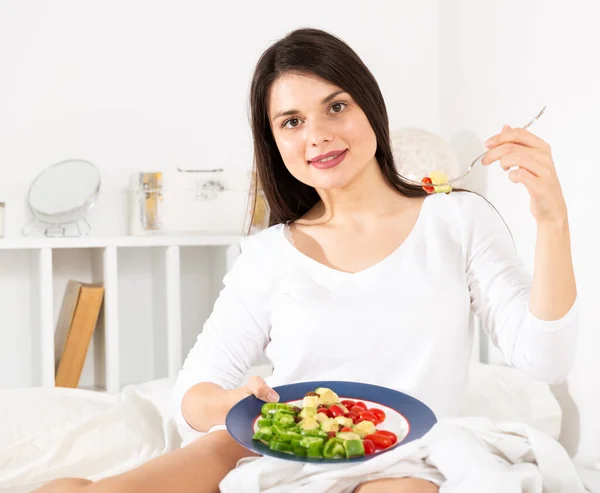 Jolie femme en robe blanche mangeant de la salade de légumes au lit — Photo