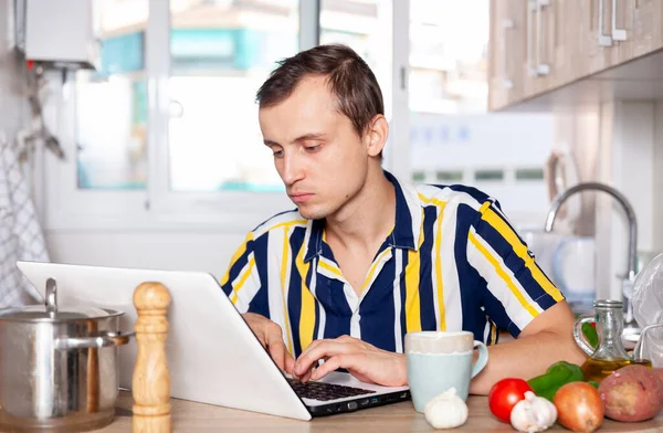 Молодой человек читает рецепт посуды в ноутбуке — стоковое фото