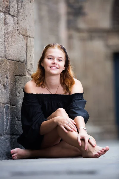 Fröhliches Mädchen sitzt barfuß an der Ziegelmauer — Stockfoto