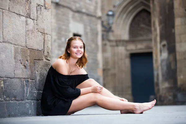 Fille gaie assise pieds nus près du mur de briques — Photo