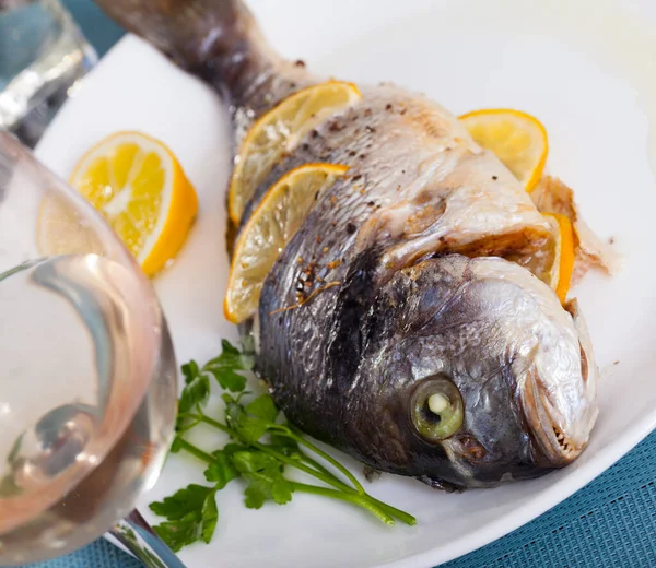 Top view of whole grilled dorada served with lemon and greens at plate — Stock Photo, Image