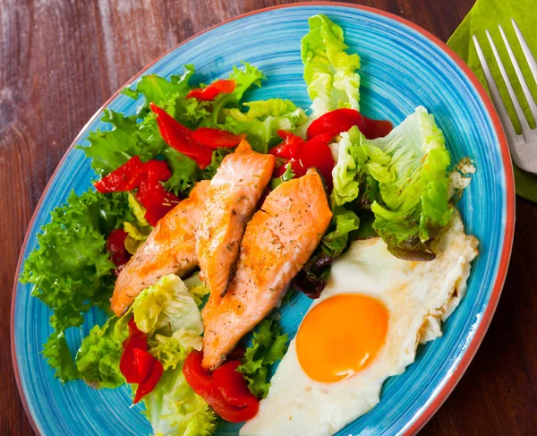 Изображение тарелки с жареной форелью, яйцом, овощами и зеленым салатом — стоковое фото
