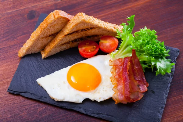 Τηγανητά αυγά με μπέικον, φρυγανισμένο ψωμί και ντομάτες στο πιάτο, αμερικάνικο πρωινό — Φωτογραφία Αρχείου