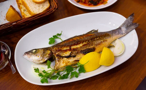 Delicious fish dish, fried bass served with onion, lemon and parsley — Stock Photo, Image